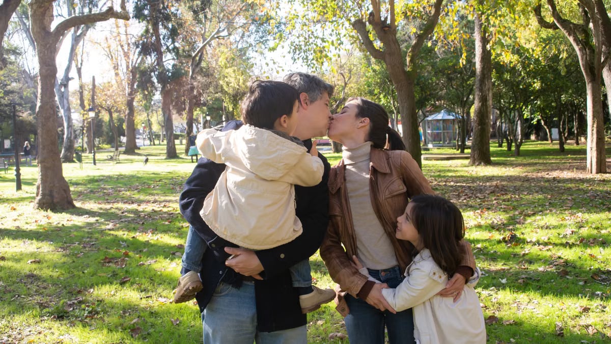 A joyful family sharing a tender moment in a sunny park setting.